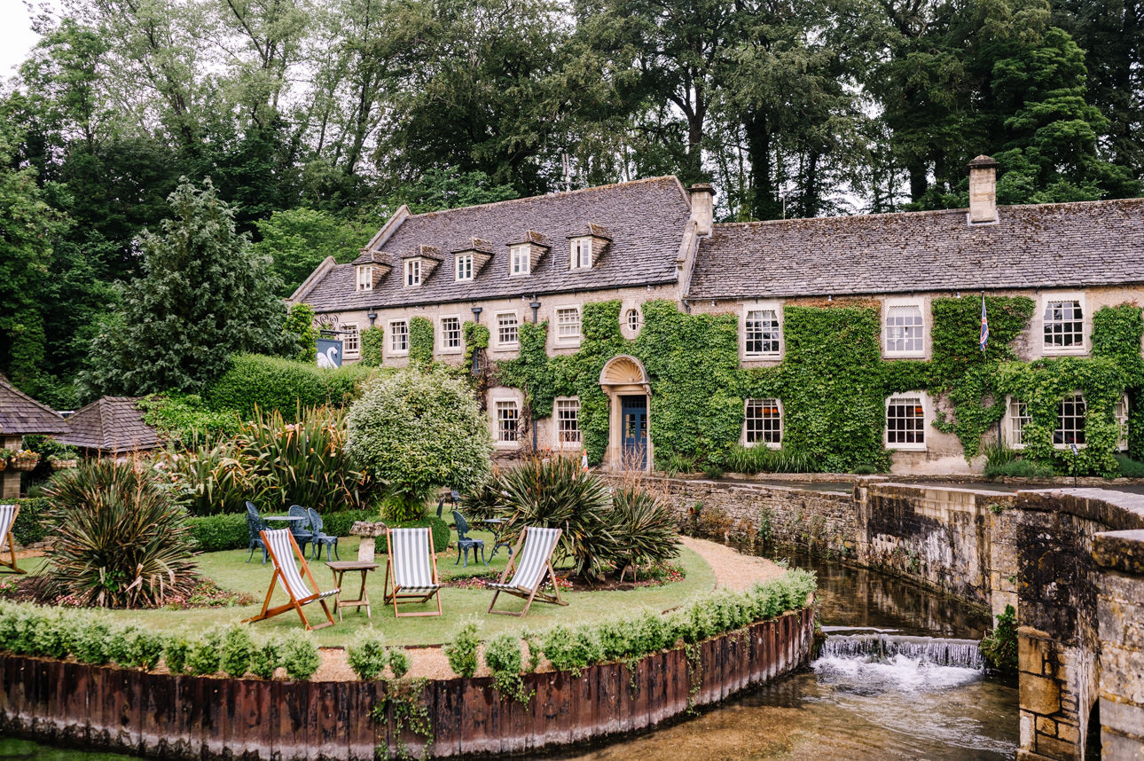 SUMMER WEDDING AT THE SWAN HOTEL BIBURY 6 Scenic view of a summer wedding at the Swan Hotel Bibury, showing the ivy-covered stone building next to the river.