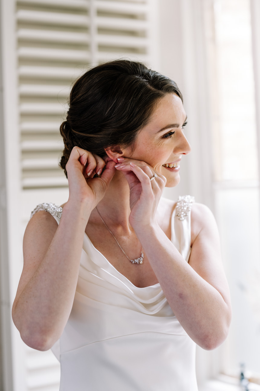 SUMMER WEDDING AT THE SWAN HOTEL BIBURY 16 Beautiful candid shot of a bride adjusting her jewelry for her summer wedding at the Swan Hotel Bibury.