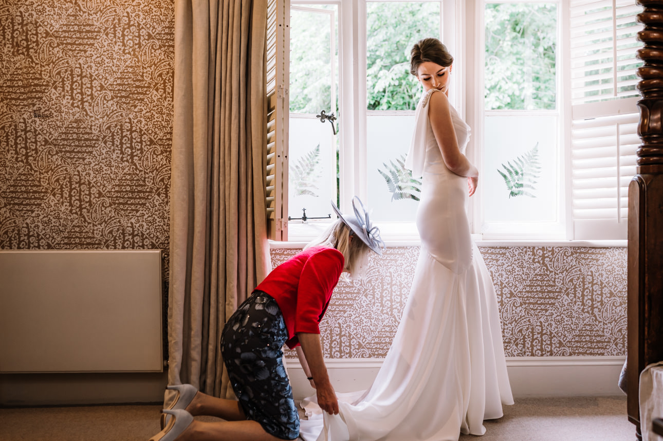 SUMMER WEDDING AT THE SWAN HOTEL BIBURY 17 Bridesmaid helping the bride adjust the train of her gown for a summer wedding at the Swan Hotel Bibury.