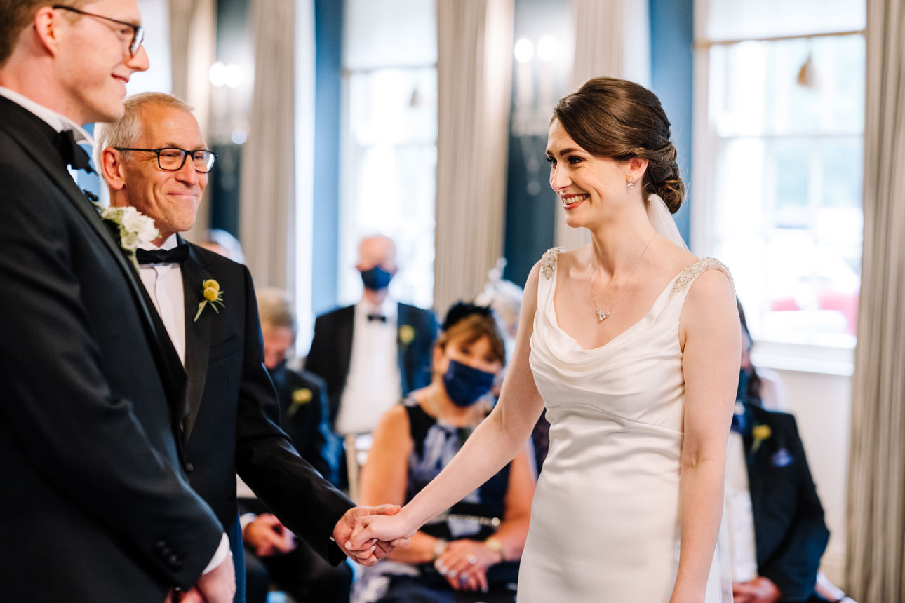 SUMMER WEDDING AT THE SWAN HOTEL BIBURY 24 Bride and groom smiling as they walk hand-in-hand down the aisle at a summer wedding at the Swan Hotel Bibury.
