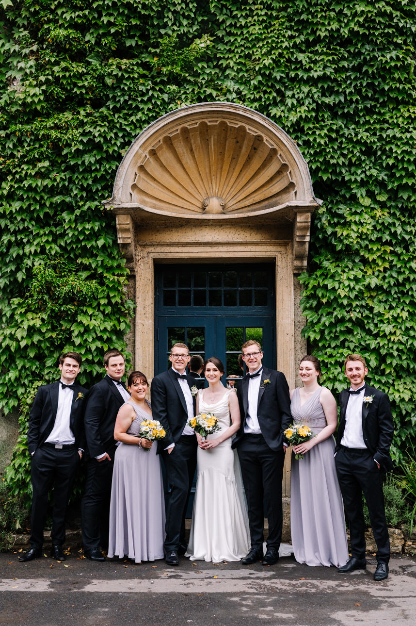 SUMMER WEDDING AT THE SWAN HOTEL BIBURY 29 Full wedding party posing outside under a grand stone archway for a summer wedding at the Swan Hotel Bibury.