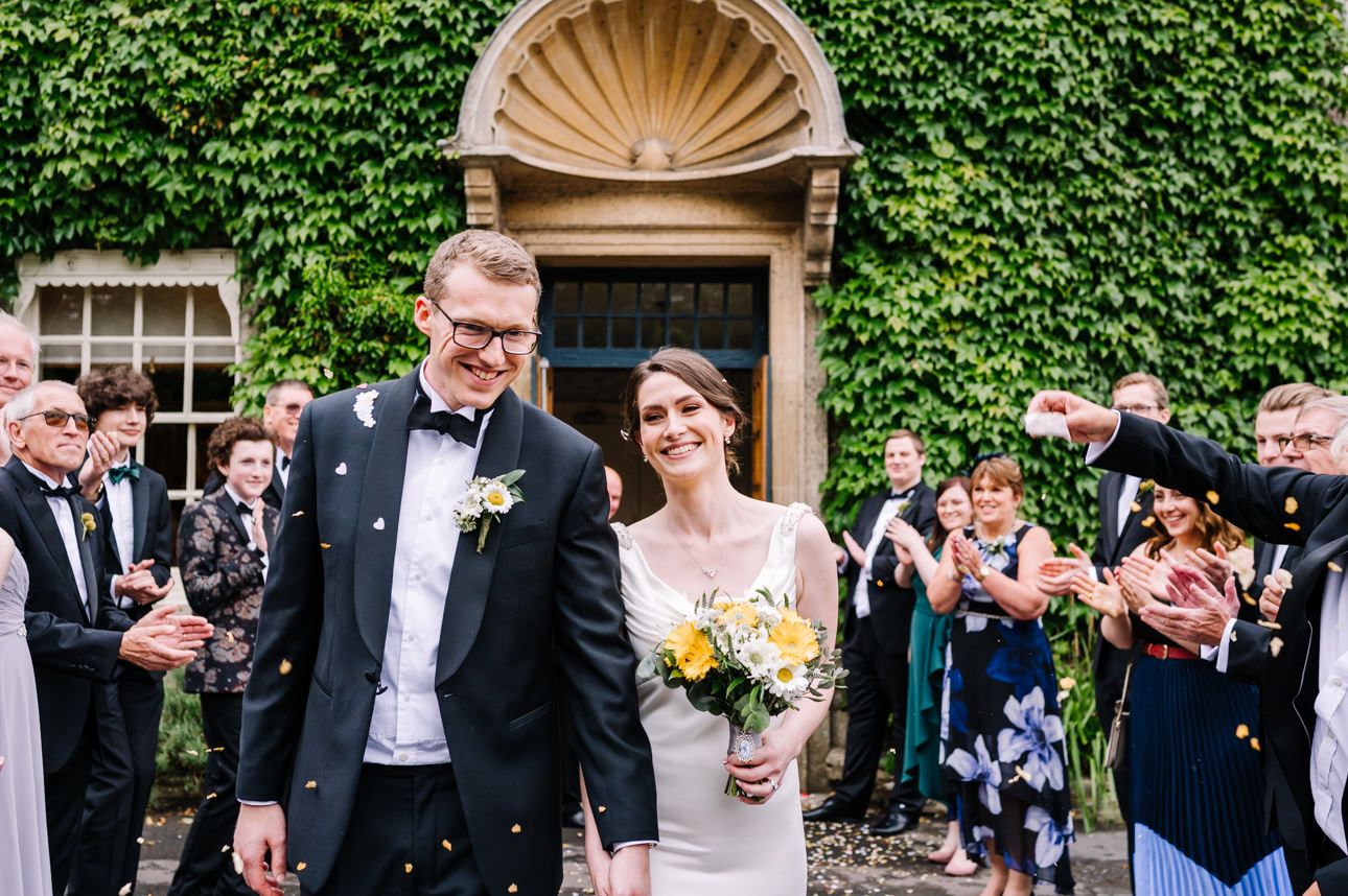 SUMMER WEDDING AT THE SWAN HOTEL BIBURY 30 Happy bride and groom walking through a shower of confetti at their summer wedding at the Swan Hotel Bibury.