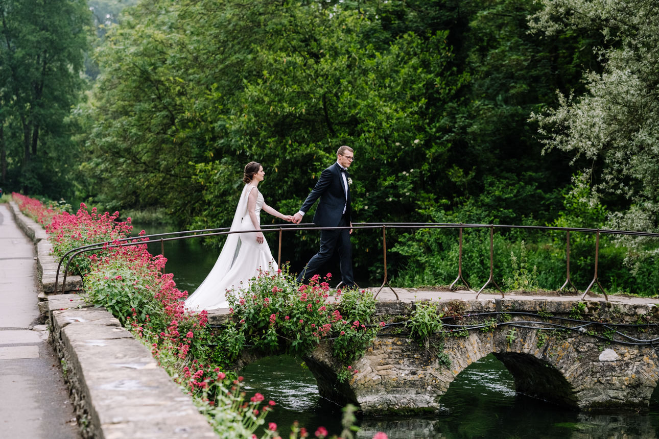 SUMMER WEDDING AT THE SWAN HOTEL BIBURY 32 Bride and groom walking along the river path during their summer wedding at the Swan Hotel Bibury.