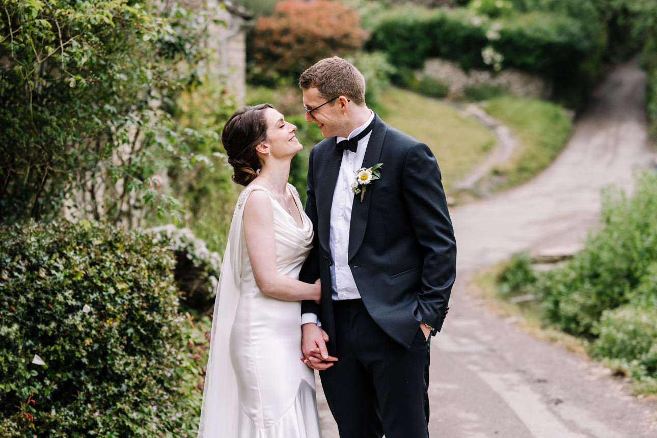 SUMMER WEDDING AT THE SWAN HOTEL BIBURY 35 Bride and groom kissing near the historic stone bridge walls during a summer wedding at the Swan Hotel Bibury.