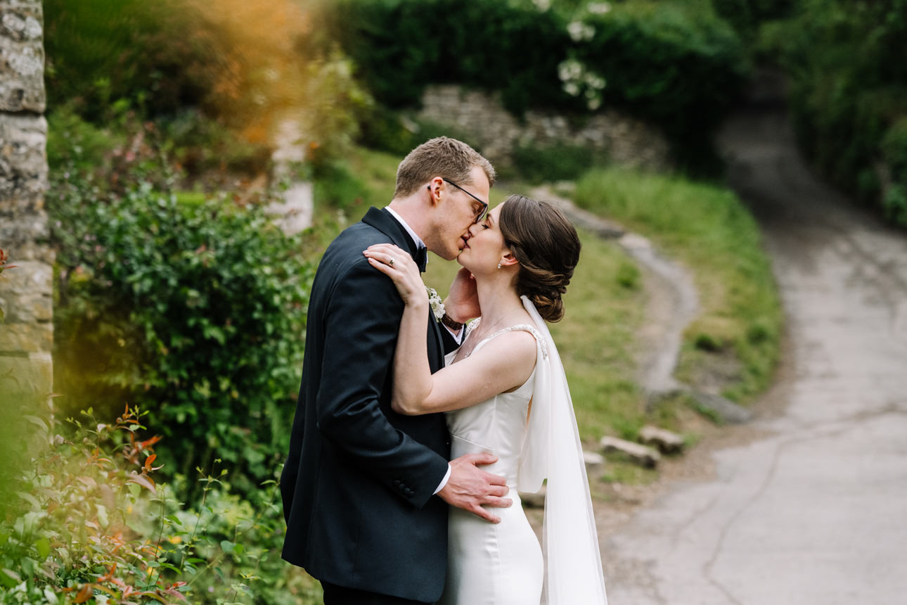 SUMMER WEDDING AT THE SWAN HOTEL BIBURY 38 Bride and groom kissing near the historic stone bridge walls during a summer wedding at the Swan Hotel Bibury.