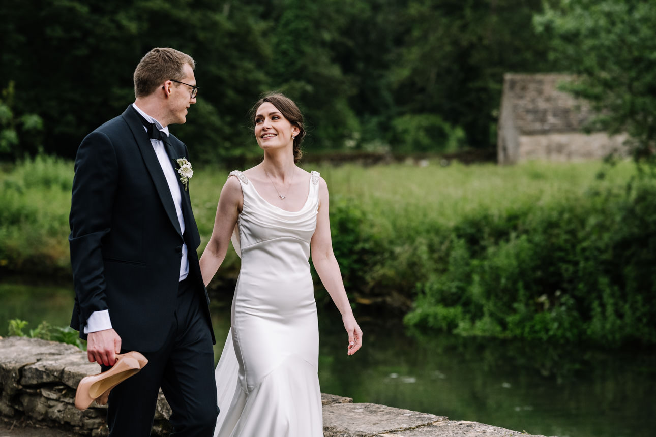 SUMMER WEDDING AT THE SWAN HOTEL BIBURY 43 Newlyweds laughing together while walking through the village at a summer wedding at the Swan Hotel Bibury.