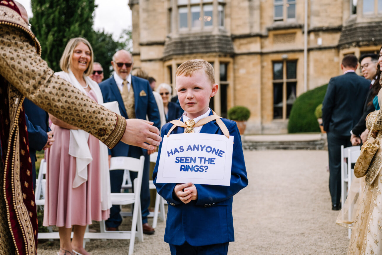 paige boy holding a sign about the wedding rings