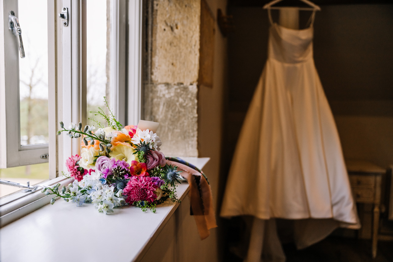LAPSTONE BARN WEDDING PHOTOGRAPHER 19 A colorful summer wedding bouquet placed next to an elegant wedding gown at Lapstone Barn.