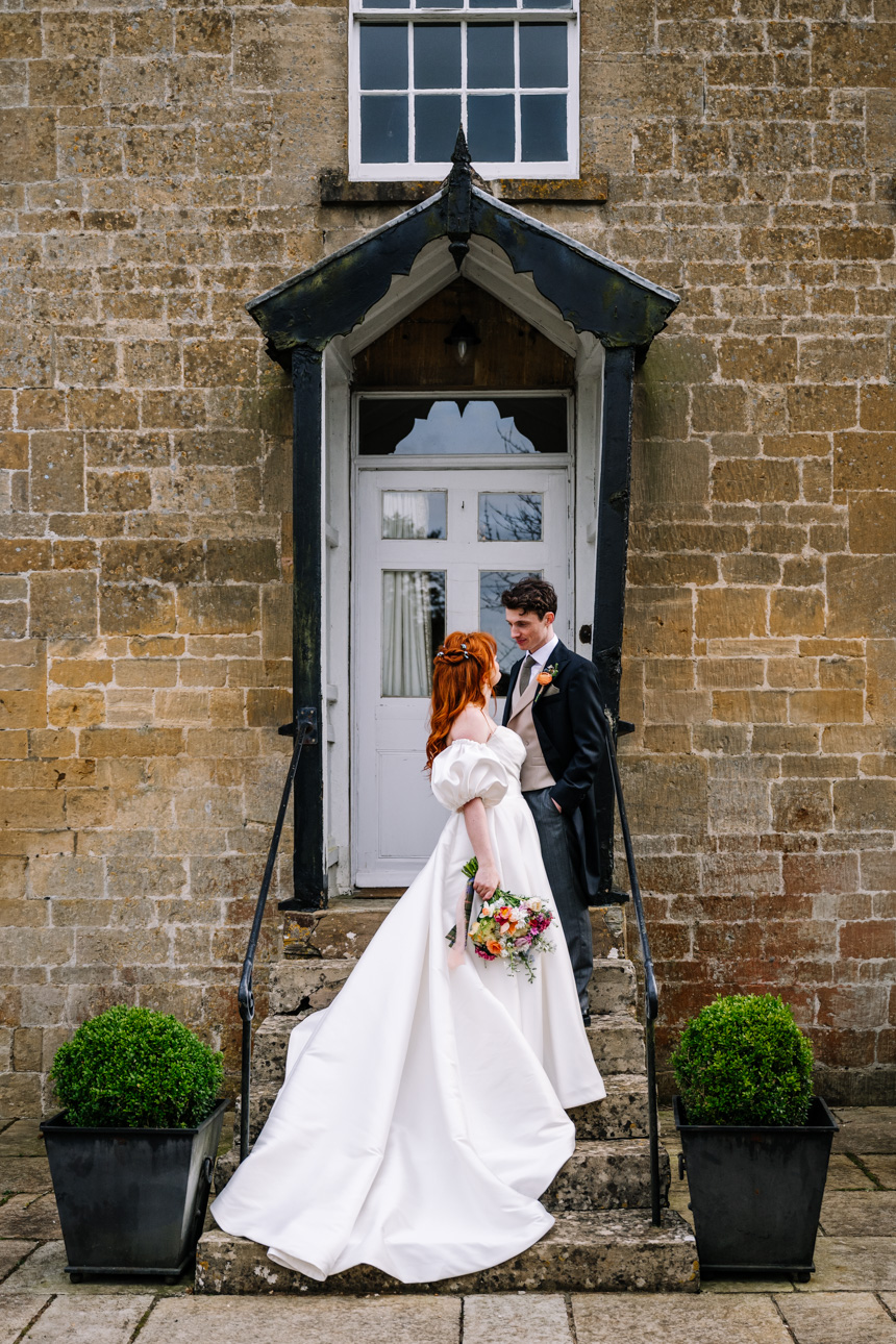 LAPSTONE BARN WEDDING PHOTOGRAPHER 59 Romantic portrait of a groom embracing his red-haired bride on a gravel path near a field at Lapstone Barn.