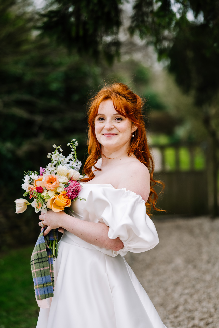 LAPSTONE BARN WEDDING PHOTOGRAPHER 60 A bride in an off-the-shoulder wedding gown standing before a historic stone arched doorway at Lapstone Barn.