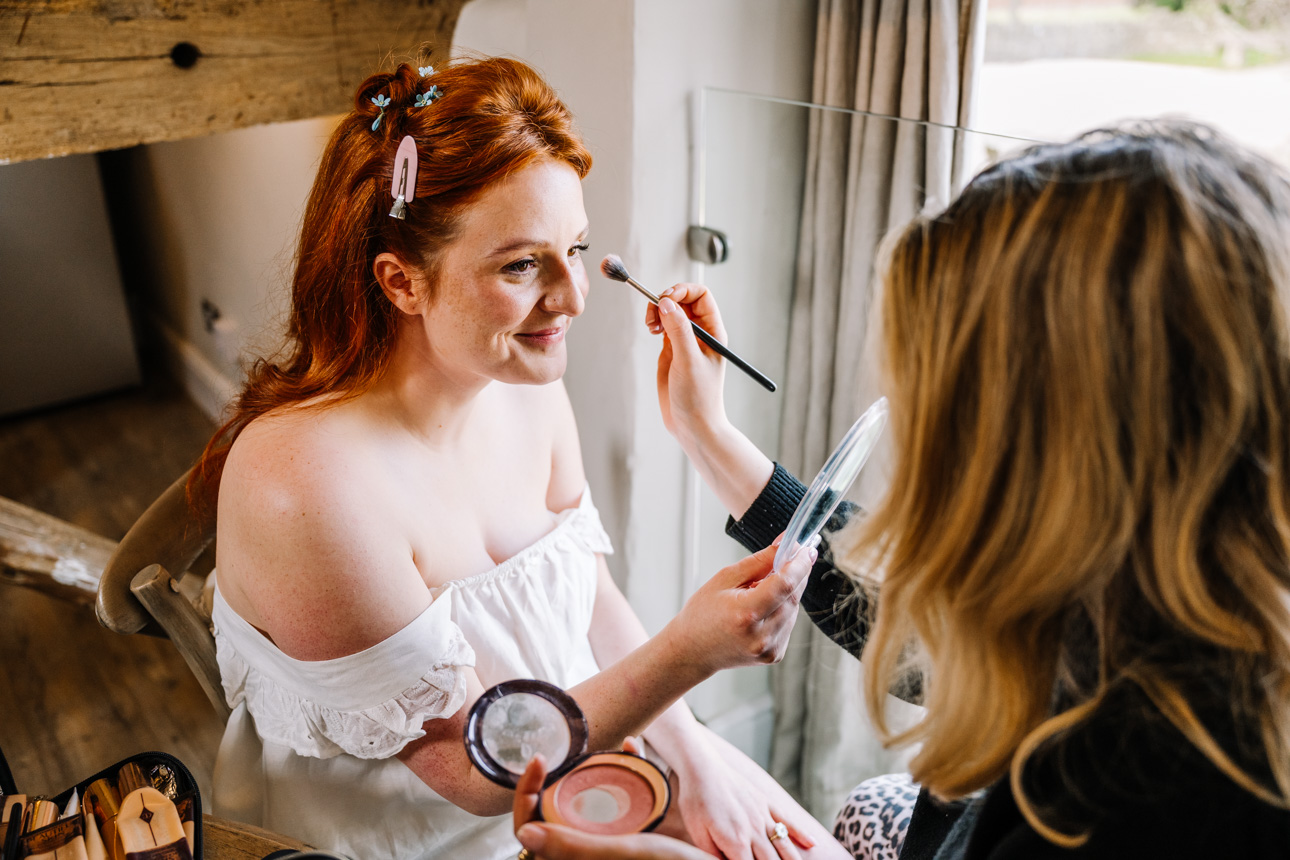 LAPSTONE BARN WEDDING PHOTOGRAPHER 20 A bride smiling while getting her makeup applied by a professional stylist before her Lapstone Barn wedding.