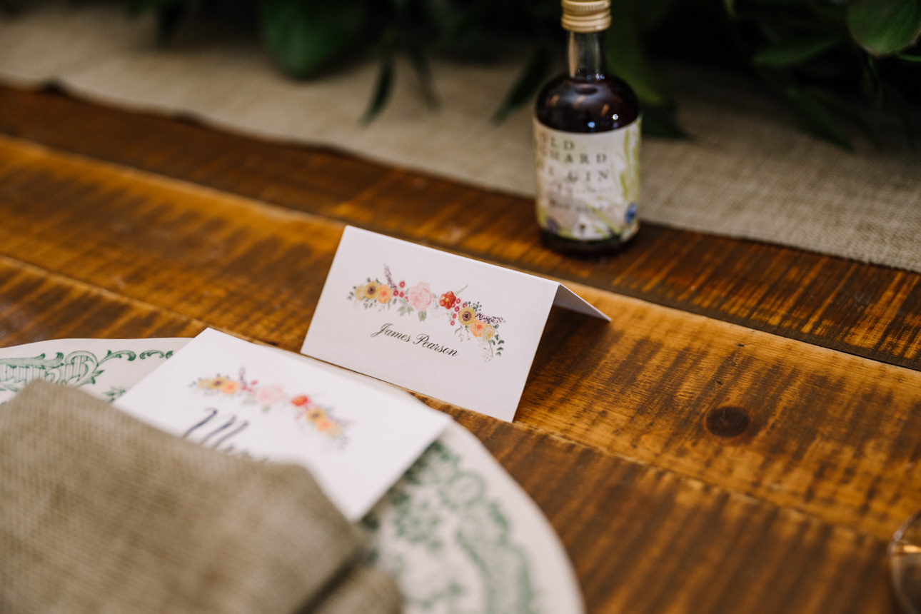 LAPSTONE BARN WEDDING PHOTOGRAPHER 76 Detailed macro shot of illustrated wedding name place cards on a wooden table at a Lapstone Barn reception.