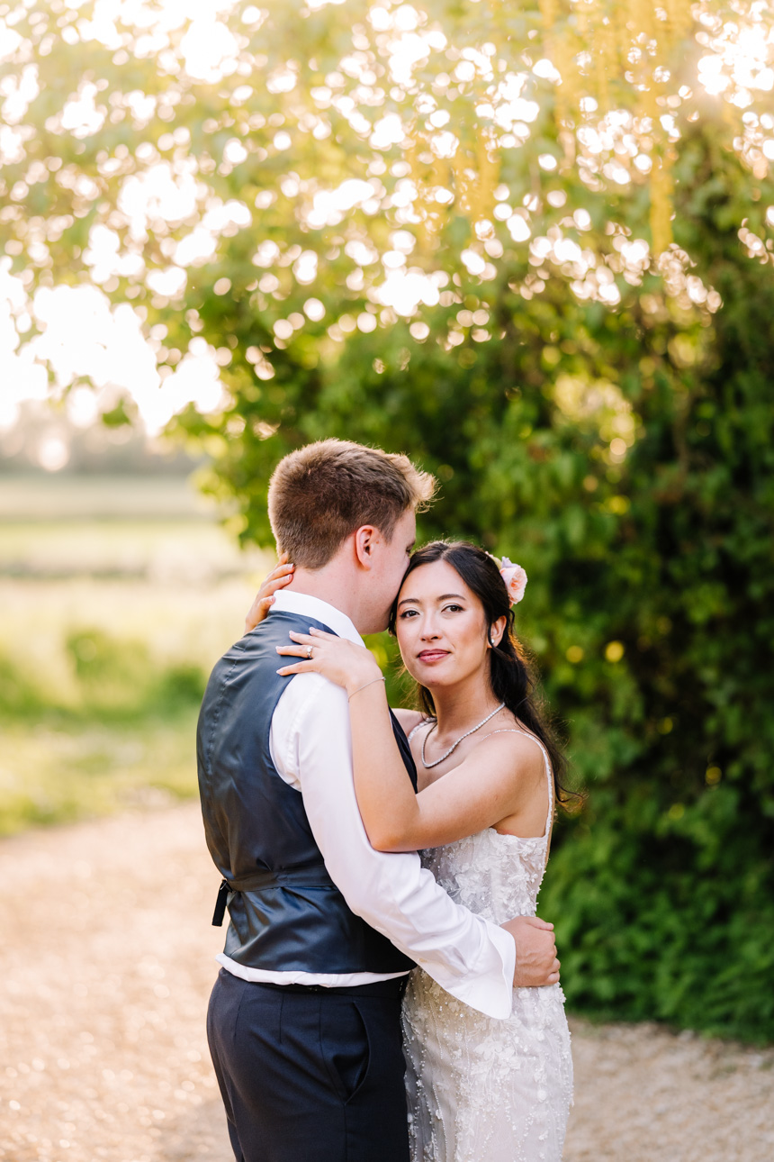 LAPSTONE BARN WEDDING PHOTOGRAPHER 45 Sun-drenched countryside wedding portrait of a bride and groom hugging, captured by Tanli Joy Weddings.