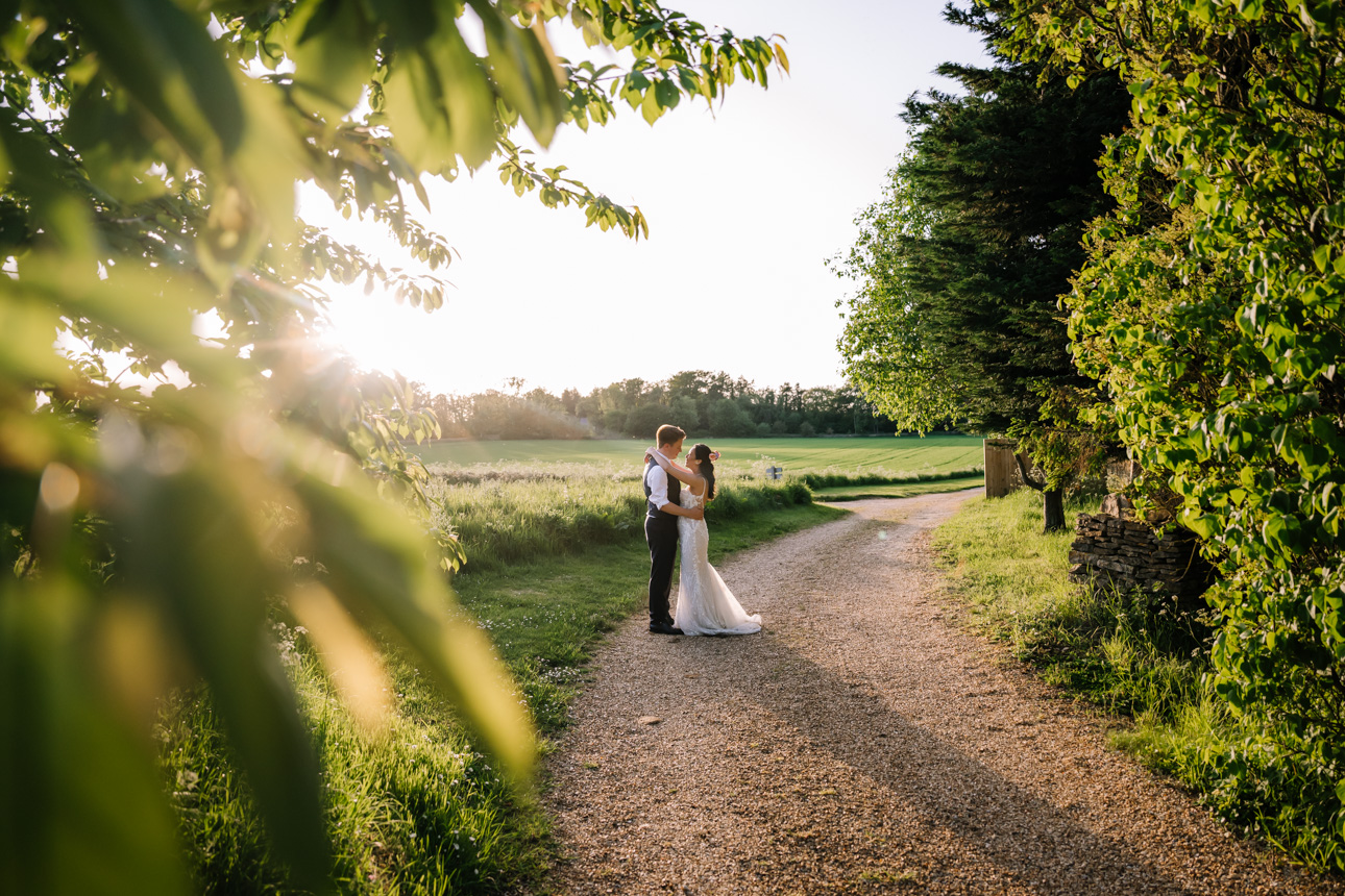 LAPSTONE BARN WEDDING PHOTOGRAPHER 70 Candid wedding photography of a newlywed couple walking through fields during a warm golden hour sunset at Lapstone Barn.