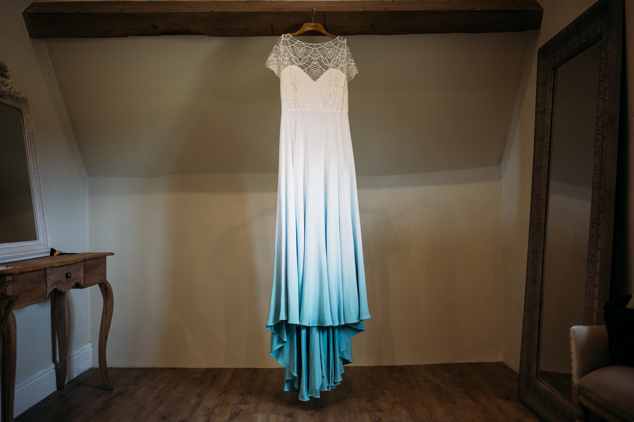 LAPSTONE BARN WEDDING PHOTOGRAPHER 15 stunning white and blue ombre wedding dress hanging against a rustic wood wall at Lapstone Barn.