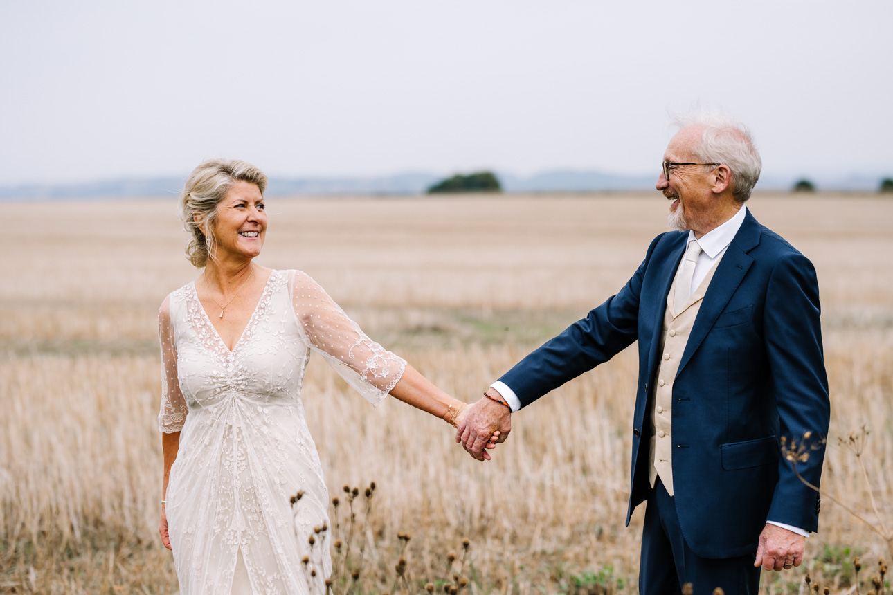 LAPSTONE BARN WEDDING PHOTOGRAPHER 94 Candid wedding photography of a bride and groom smiling and holding hands while walking in an open field at Lapstone Barn.