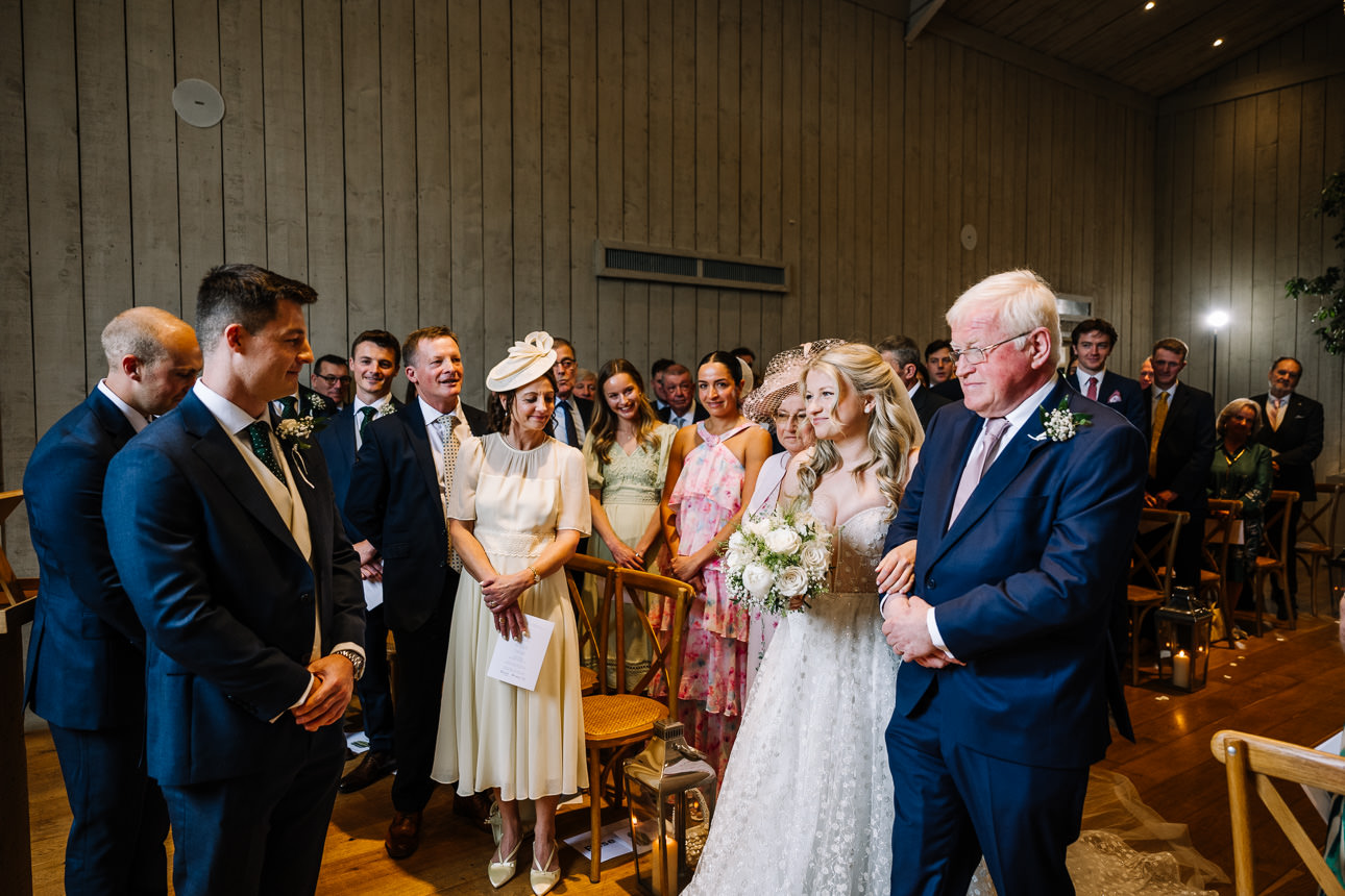 FLORA AND WILLIAM PRIMROSE HILL FARM SPRING WEDDING 23 Bride walking down the aisle with her father as guests watch