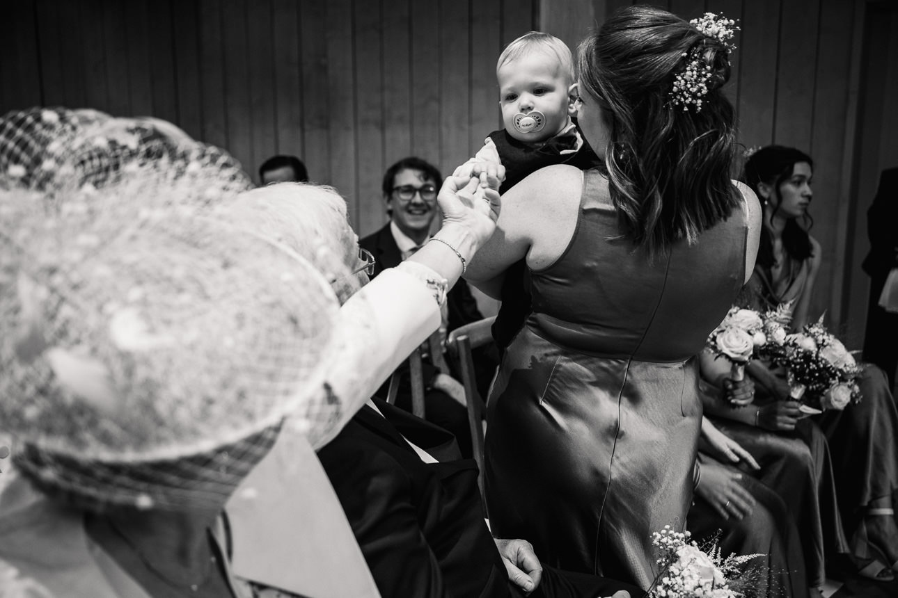 FLORA AND WILLIAM PRIMROSE HILL FARM SPRING WEDDING 34 Young child being held during the wedding celebrations in black and white