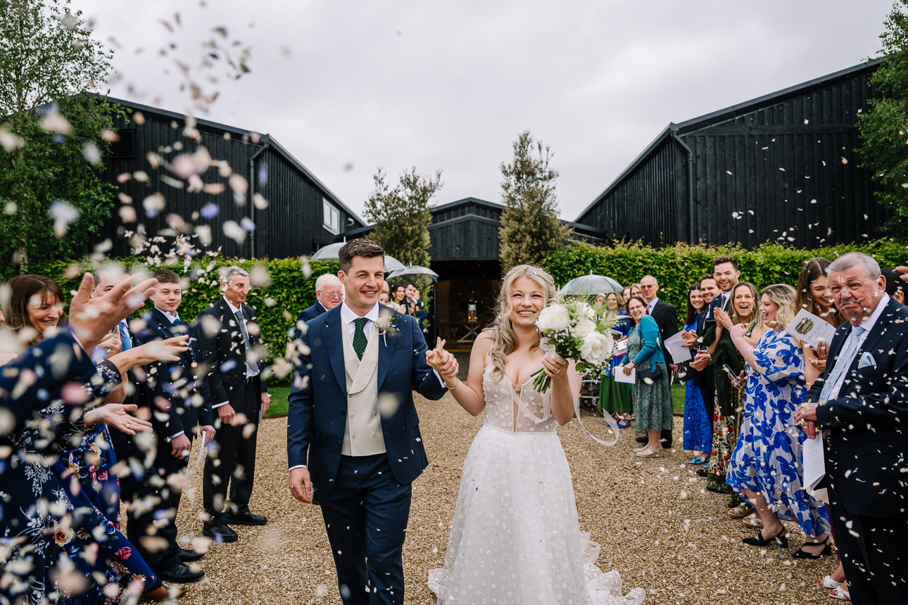 FLORA AND WILLIAM PRIMROSE HILL FARM SPRING WEDDING 37 Happy wedding guests throwing colourful confetti over the newly married couple