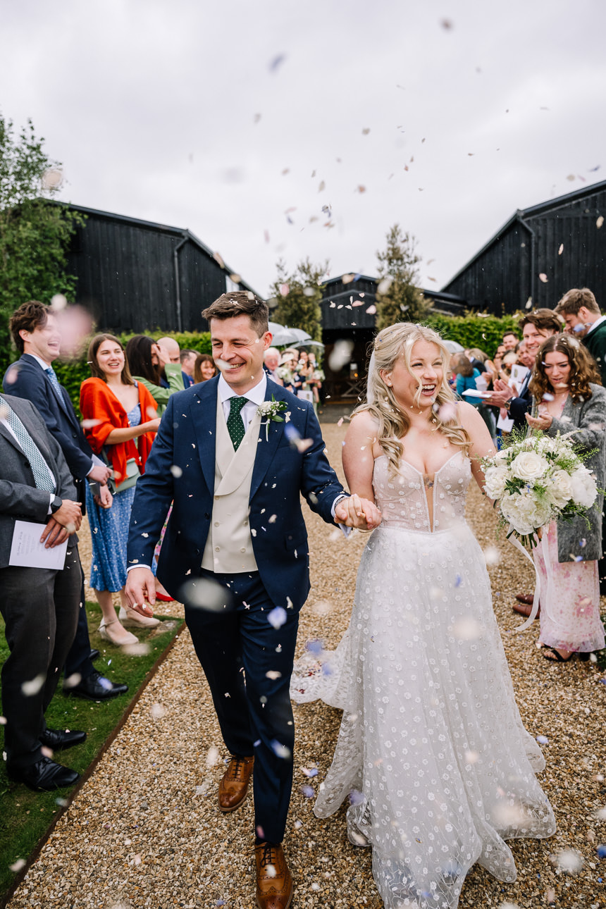 FLORA AND WILLIAM PRIMROSE HILL FARM SPRING WEDDING 38 Bride and groom walking through confetti with their wedding guests celebrating around them