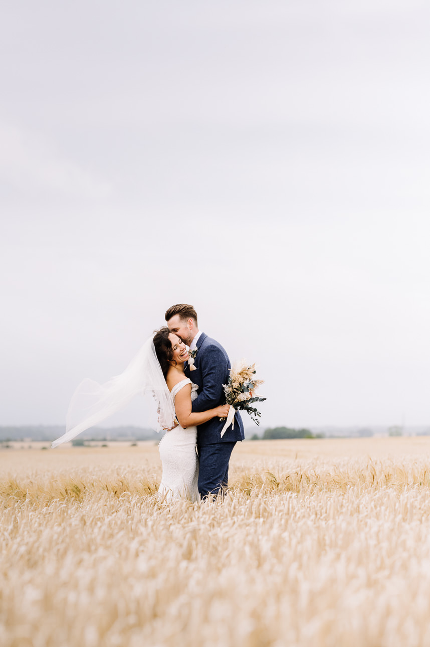 NATURAL WEDDING PHOTOGRAPHY 45 A bride and groom sharing a tender, natural embrace while standing in an open field under soft, airy skies.