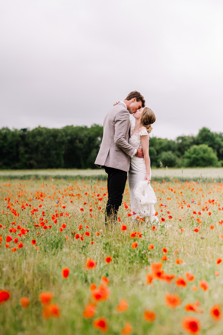 NATURAL WEDDING PHOTOGRAPHY 46 An elegant couple sharing a romantic embrace while standing in a vibrant red poppy and wildflower field.