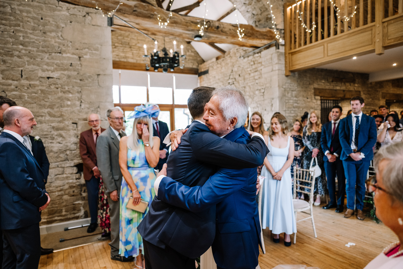 GREAT TYTHE BARN WEDDING PHOTOGRAPHER 24 emotional embrace with a wedding guest inside the rustic stone reception space at The Great Tythe Barn.