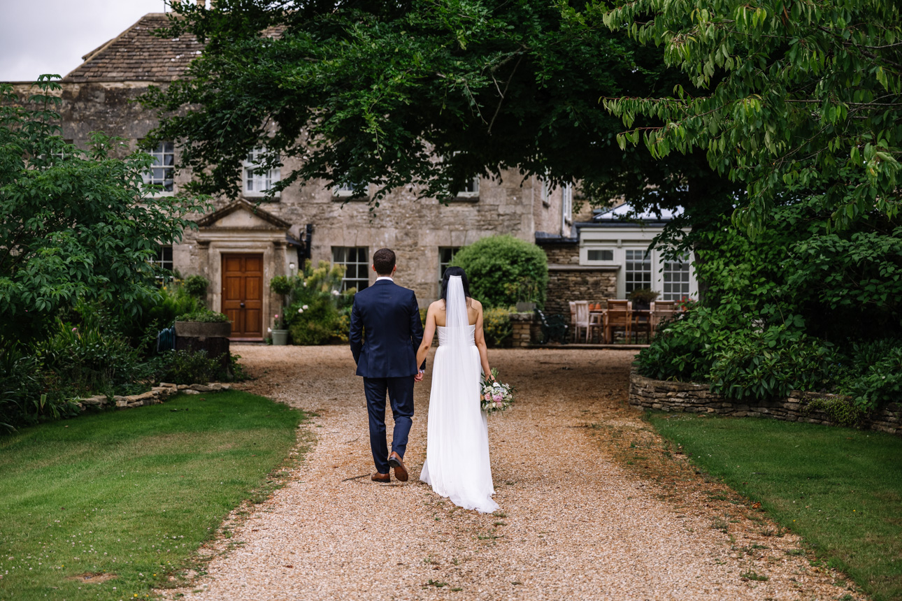 GREAT TYTHE BARN WEDDING PHOTOGRAPHER 57 Greg and Chloe holding hands and walking down a rustic driveway lined with trees at The Great Tythe Barn.