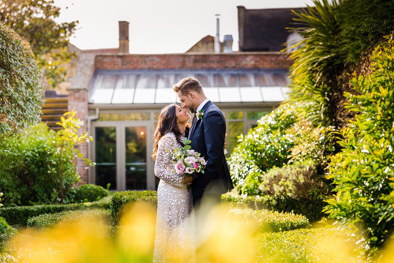 NATURAL WEDDING PHOTOGRAPHY 47 A bride and groom sharing a relaxed, natural portrait session outside a historic Cotswold stone manor house with beautiful green gardens.