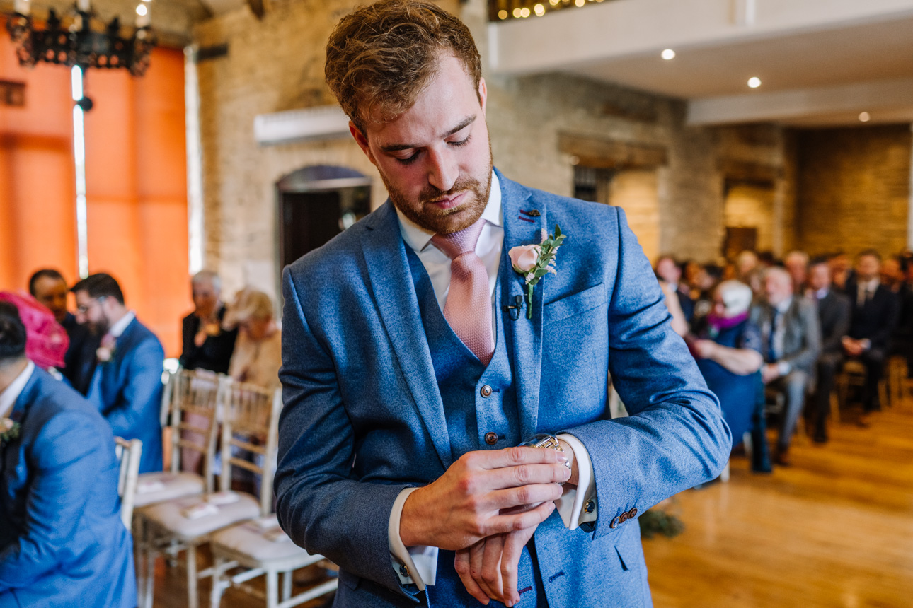 GREAT TYTHE BARN WEDDING PHOTOGRAPHER 29 A candid portrait of groom Perry adjusting his cufflinks inside the light-filled preparation room at The Great Tythe Barn.