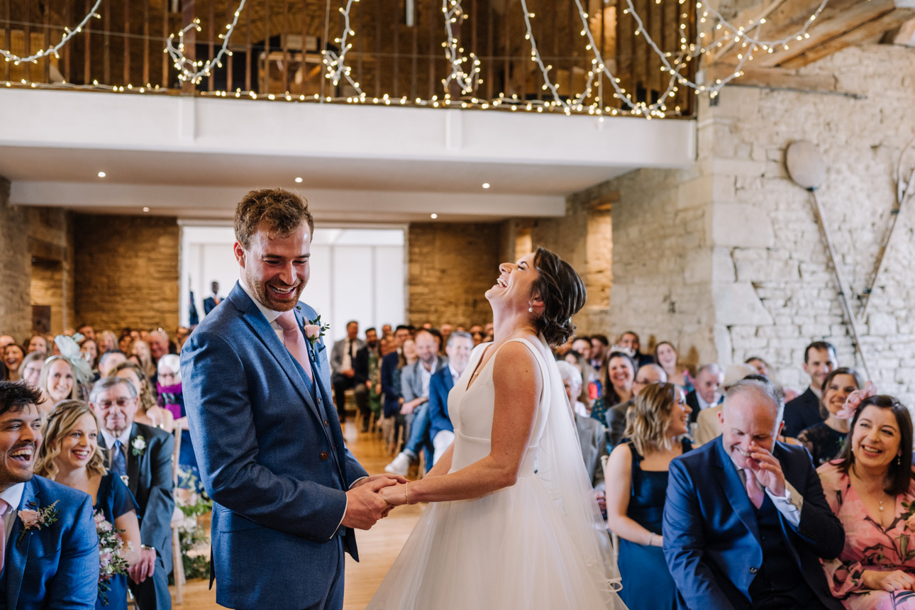 GREAT TYTHE BARN WEDDING PHOTOGRAPHER 30 couple laughing during their wedding ceremony at the great tythe barn in tetbury.