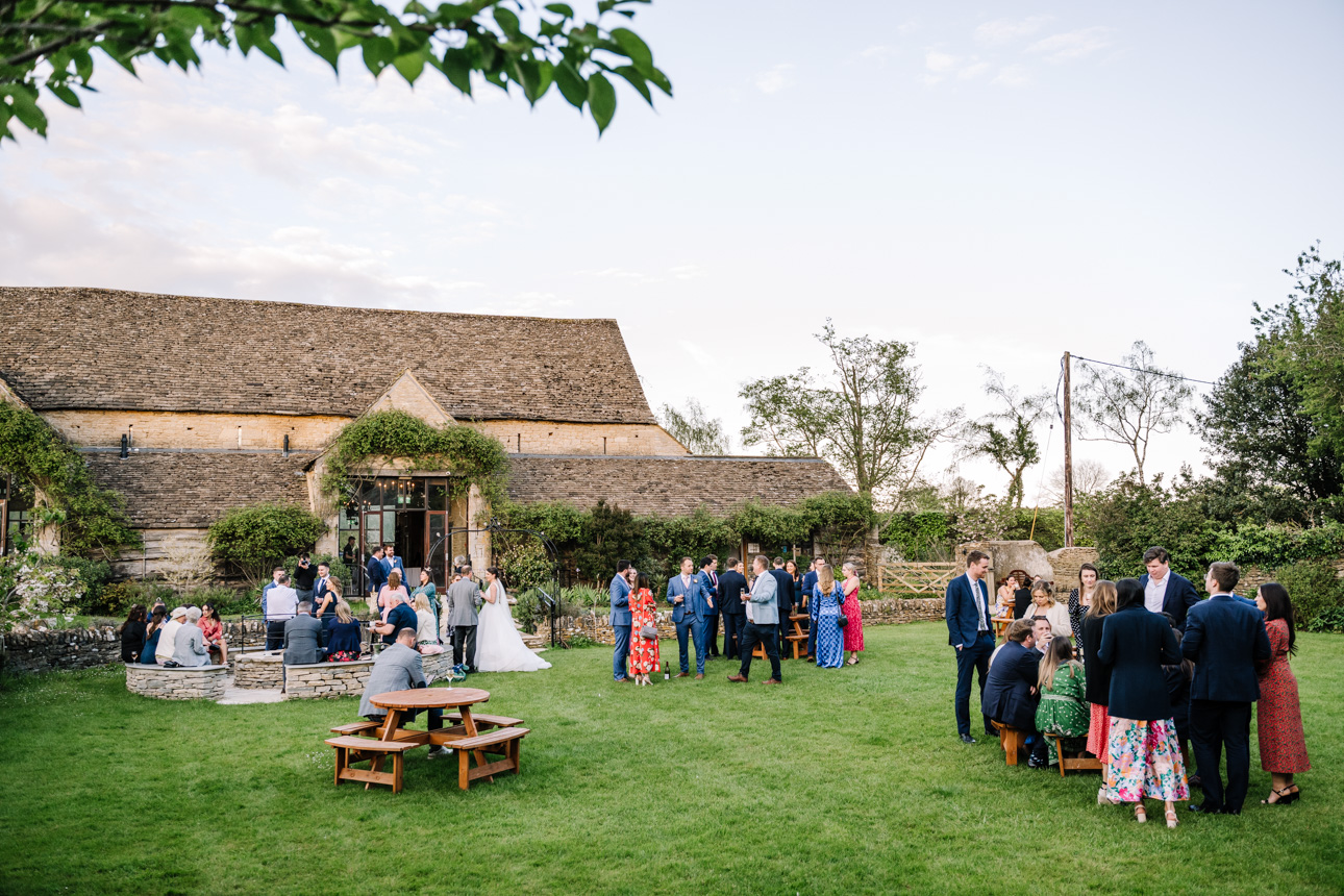 GREAT TYTHE BARN WEDDING PHOTOGRAPHER 97 Wedding guests mingling and drinking on the expansive green lawns during a summer afternoon reception at The Great Tythe Barn.