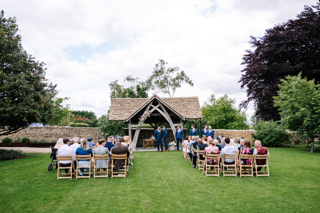 GREAT TYTHE BARN WEDDING PHOTOGRAPHER 39 A wide-angle photograph capturing Rachel and Leigh's outdoor civil ceremony taking place under the sunny skies at The Great Tythe Barn.