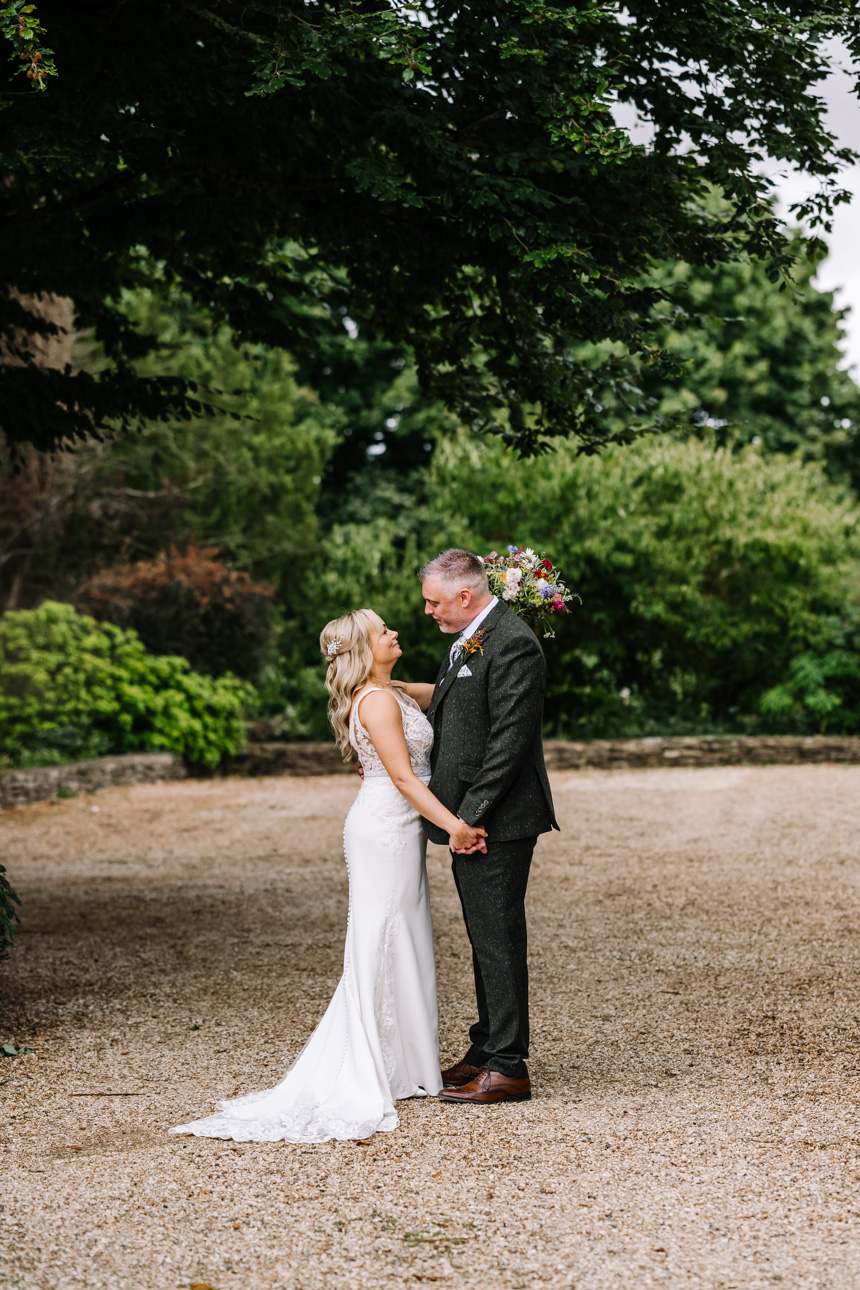 GREAT TYTHE BARN WEDDING PHOTOGRAPHER 1 A bride in a lace wedding dress and a groom in a dark suit standing outside the historic stone entrance of The Great Tythe Barn.