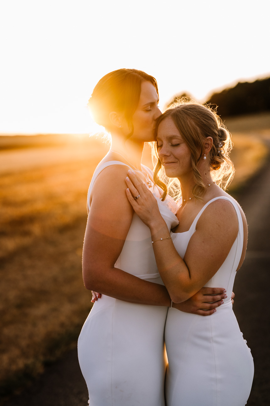 KINGSCOTE BARN WEDDING PHOTOGRAPHER 83 golden hour at Kingscote barn showing 2 brides walking hand in hand into the sunset