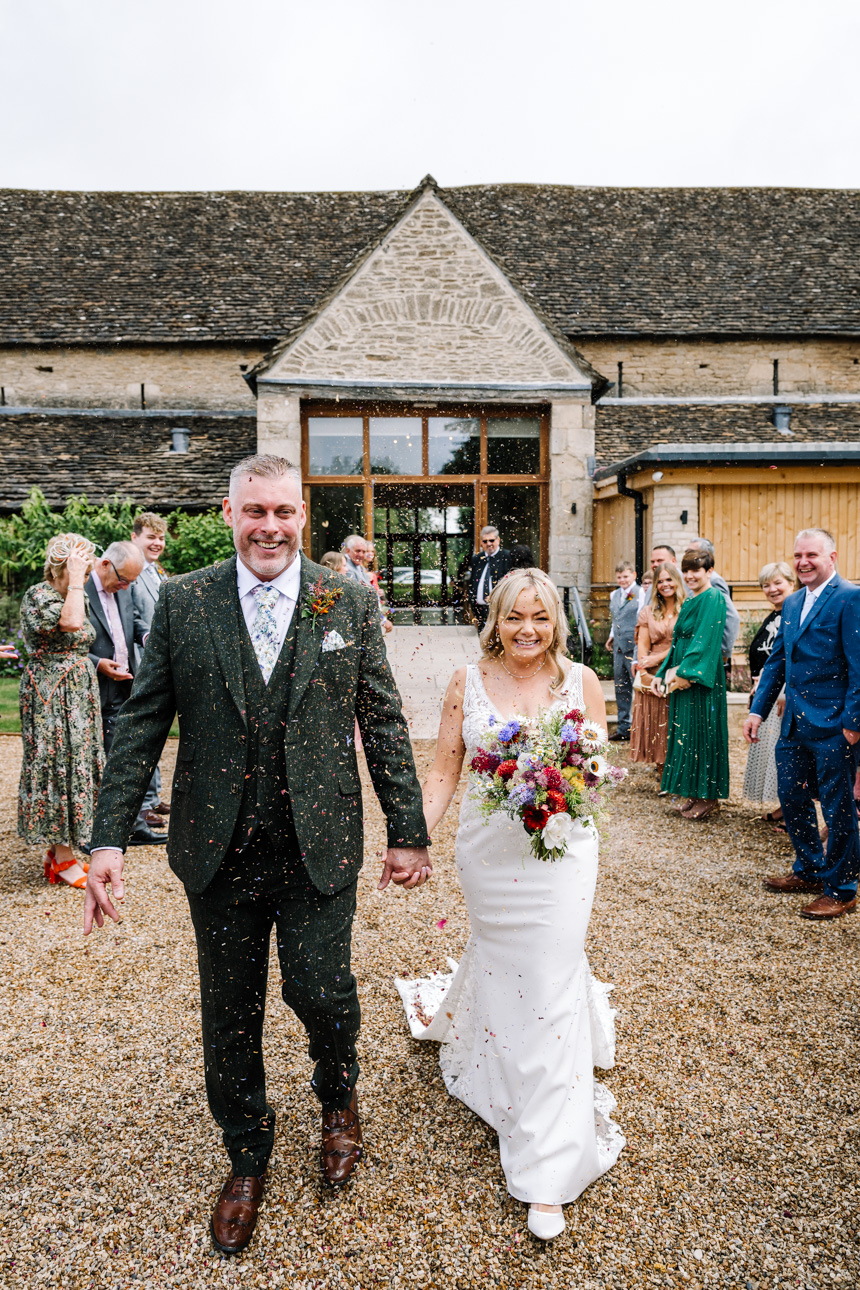 GREAT TYTHE BARN WEDDING PHOTOGRAPHER 116 A smiling bride and groom walking together past the traditional stone buildings during their wedding day at The Great Tythe Barn.