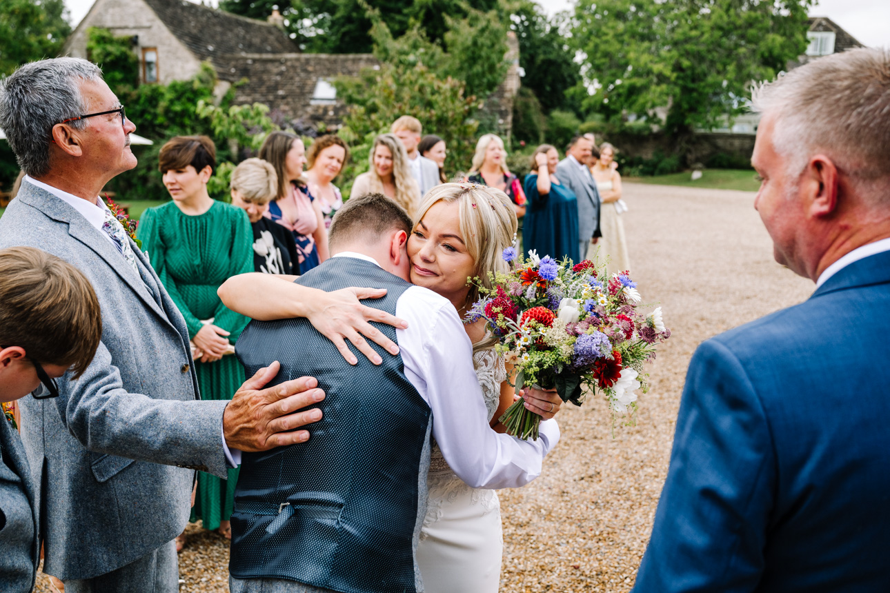 GREAT TYTHE BARN WEDDING PHOTOGRAPHER 9 An emotional close-up candid photo of a bride hugging a wedding guest on the courtyard lawns at The Great Tythe Barn.