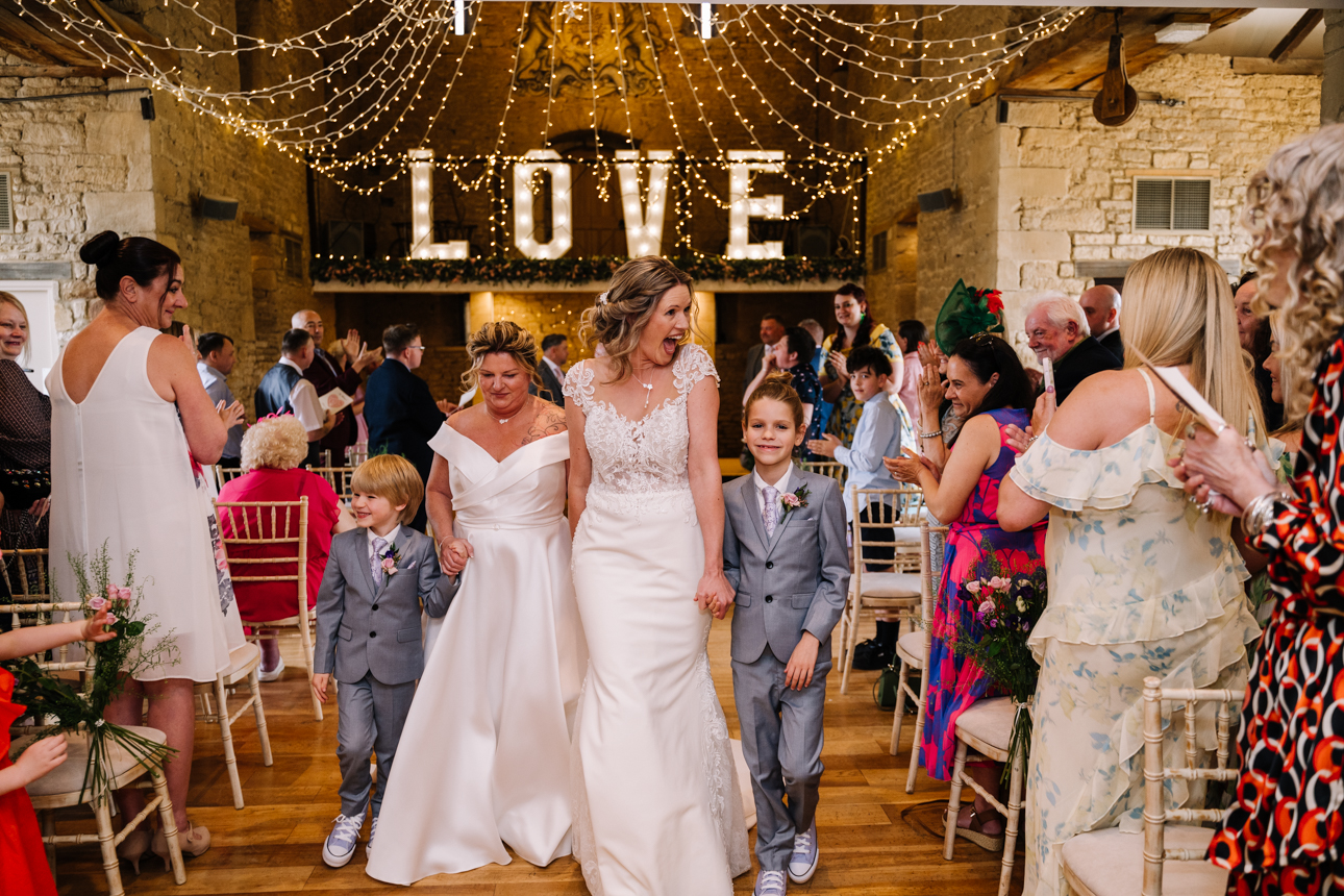 GREAT TYTHE BARN WEDDING PHOTOGRAPHER 33 two brides exiting their wedding ceremony at the great tythe barn.