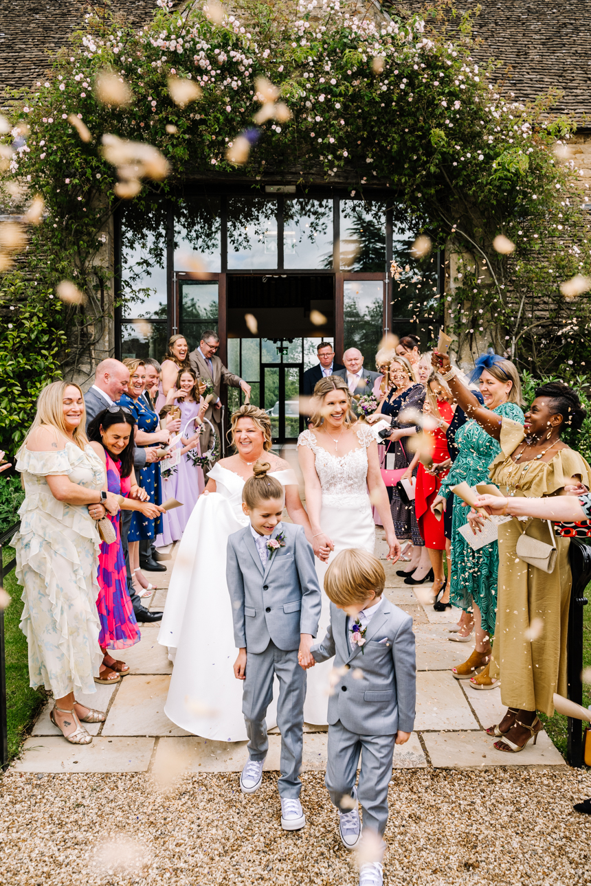 GREAT TYTHE BARN WEDDING PHOTOGRAPHER 14 A massive crowd of wedding guests cheering and celebrating as they throw confetti outside the stone walls of The Great Tythe Barn.